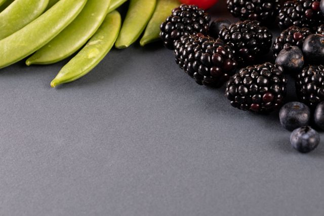 This image showcases a high angle close-up of fresh blackberries, blueberries, and green peas on a gray background. Ideal for use in articles, blogs, and advertisements related to organic food, healthy eating, nutrition, vegan and vegetarian diets, and clean eating. Perfect for promoting natural produce and raw food recipes.