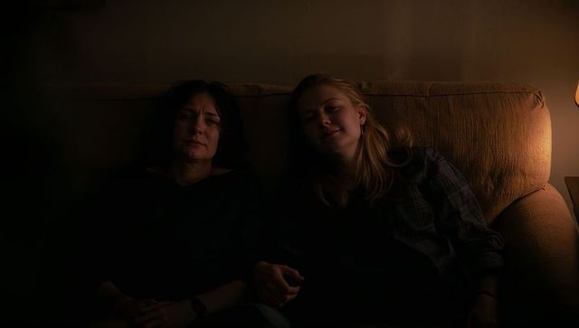 Two women relaxing on sofa in soft amber lamp glow moody intimate evening