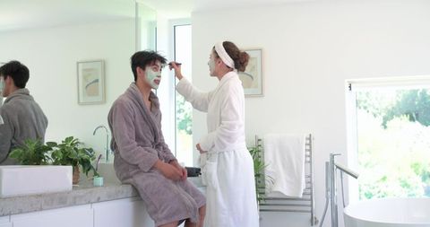 Asian man and african american woman sharing playful skincare routine in bright bathroom