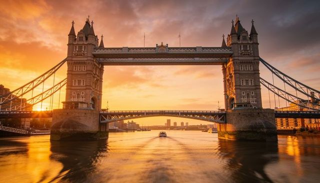 Golden-hour tower bridge panorama with glowing towers, river reflections and passing boat
