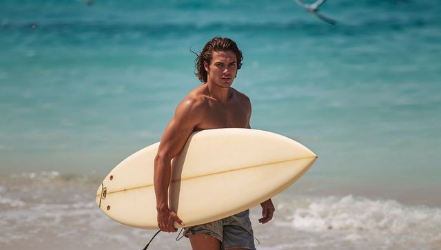 Shirtless Male Surfer Carrying Cream Shortboard on Turquoise Beach, Active Summer Lifestyle