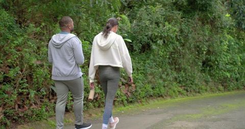African american couple walking along lush forest trail holding water bottle and phone