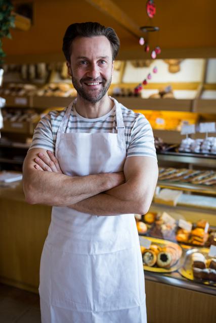 Portrait of smiling owner standing in bakery shop with his hands crossed