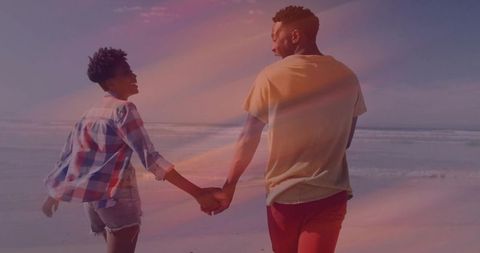 Couple Holding Hands Walking Along Sunny Beach