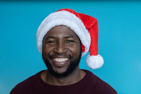 Smiling african american man wearing santa hat spreading holiday cheer on turquoise backdrop