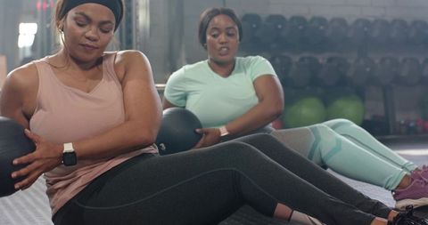 Medicine ball core workout with two women wearing smartwatches in gym studio