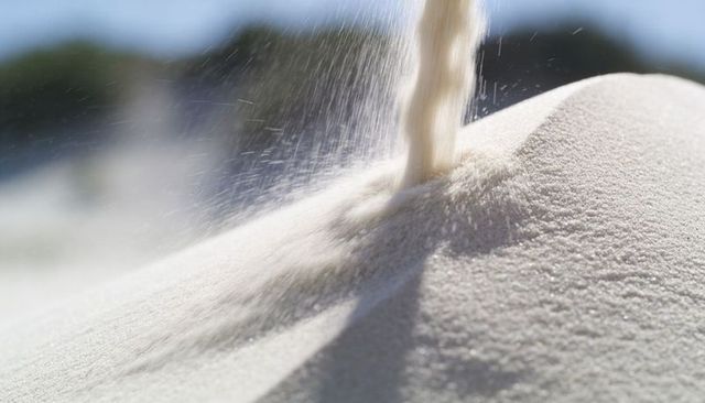 Sunlit fine sand pouring, forming textured dune ridge closeup, flowing grains macro