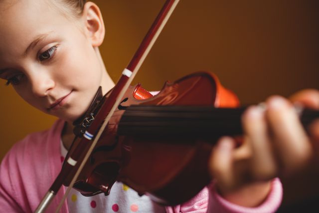 Young girl playing violin with a focused expression on a yellow background. Ideal for use in educational materials, music school promotions, articles on childhood development and learning, or advertisements for musical instruments and lessons.