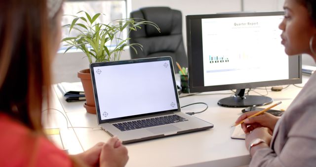 Two professionals collaborating in a modern office, using a laptop and reviewing documents on a monitor. Suitable for business, teamwork, project planning, and office workspace themes. Ideal for websites, presentations, and marketing materials focusing on corporate work environment.