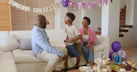 African American family celebrating son's birthday at home with cupcakes, balloons, gifts