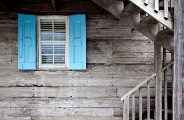 Rustic wooden house with blue shutters beside a stairway. Ideal for articles on farmhouse decor, rustic living, and countryside architecture. Suitable for background in real estate, travel blogs, and design inspiration.