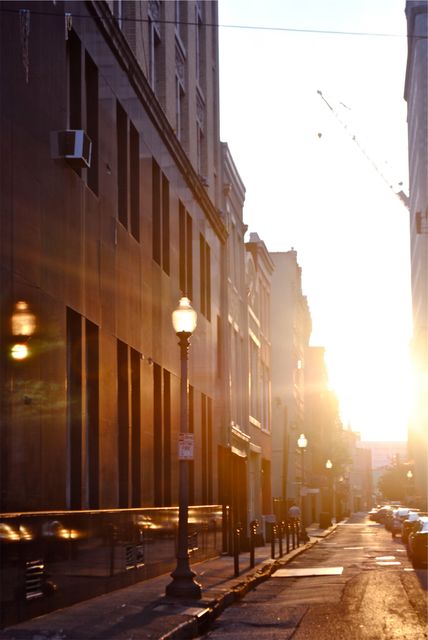 Sunrise illuminating a quiet city street with modern buildings and a lamp post. Ideal for showcasing urban morning scenes, city architecture, or creating a calm, early morning mood in urban settings. Suitable for backgrounds, travel blogs, and architectural features.