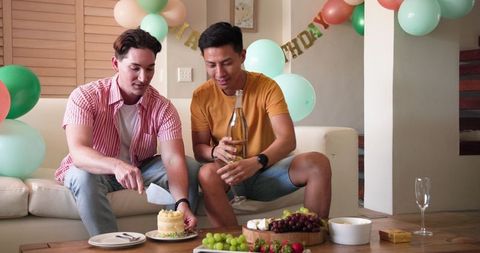 Celebrating birthday with cake and wine, joyful gay couple at home