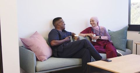 Healthcare team taking coffee break in clinic lounge, chatting on sofa, smiling together