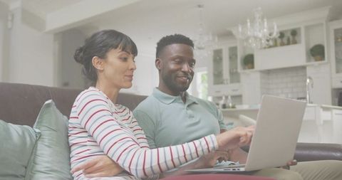 Couple browsing laptop together on couch, collaborating at home in bright modern kitchen
