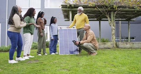 Multigenerational family watching solar technician demonstrating panel and meter outdoors