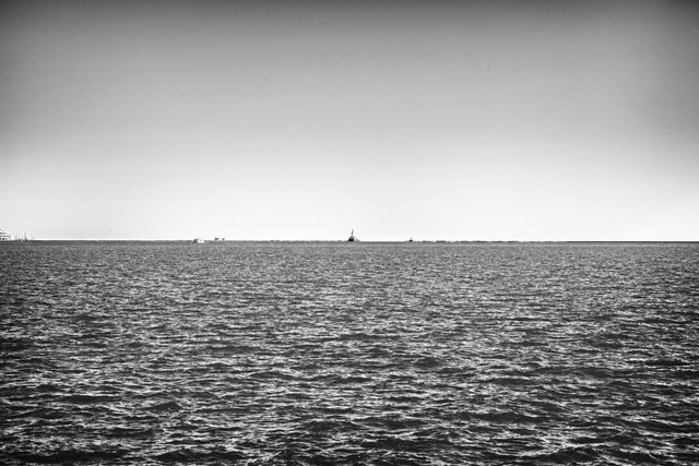 Shows a vast ocean with calm waters in monochrome, with a barely visible statue on the horizon. Can be used for backgrounds, posters searching for a sense of calm and vastness, or articles discussing travel and exploration.