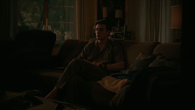 Contemplative man sitting on sofa folding hands moody backlit living room evening