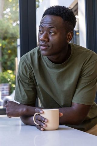 African american man holding mug at kitchen counter gazing toward window