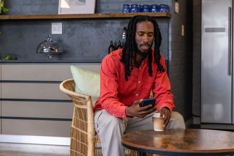 African american man sitting in cafe with smartphone and coffee wearing red shirt