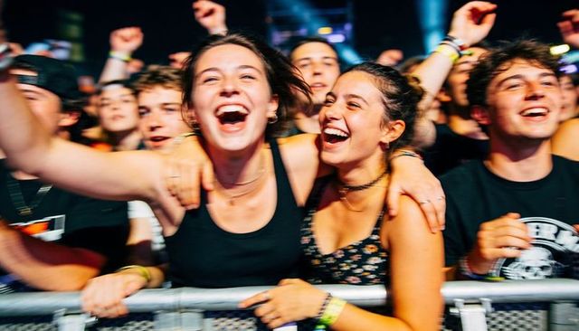 Front row friends cheering, laughing and celebrating at live concert festival together