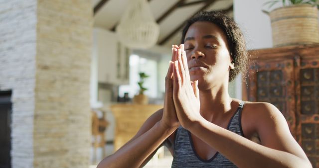 This image shows a woman in a peaceful home environment practicing meditation with hands in prayer position. Ideal for use in articles, websites, or promotional materials focused on mindfulness, mental health, relaxation, and well-being.