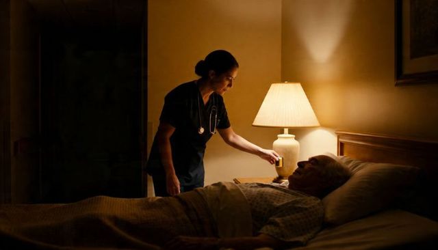 Night nurse adjusting bedside lamp while checking elderly patient resting in hospital bed