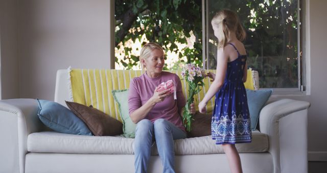 Young girl gifting vase of flowers to mother on living room couch - Download Free Stock Images Pikwizard.com