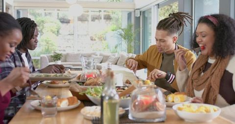 Diverse friends enjoying relaxed lunch around wooden table in sunlit modern home