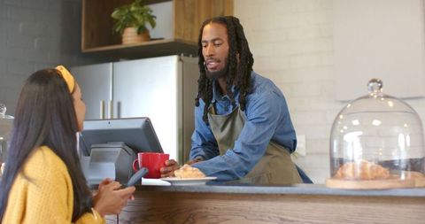 Barista handing red mug and croissant to customer at cozy rustic coffeehouse counter, hospitality