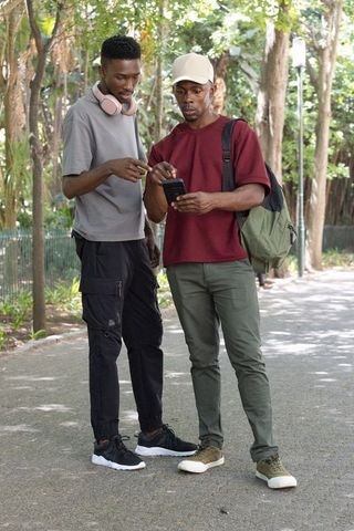 Two african men sharing smartphone on park walkway, casual urban friendship and navigation moment