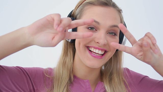 This video depicts a joyful blonde woman dancing and smiling against a white background while wearing headphones. Great for use in advertisements, websites, or social media posts involving happiness, music, personal expression, lifestyle, or youth culture.