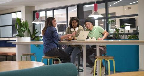 African American team collaborating over laptop in modern coworking space with plants