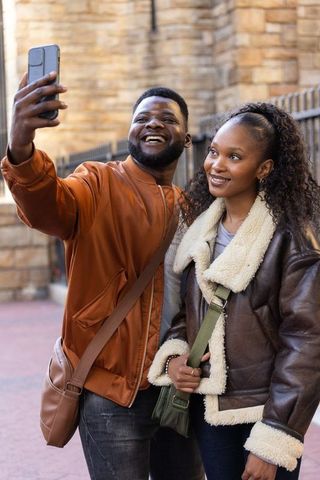 Couple taking selfie laughing on city street in warm coats