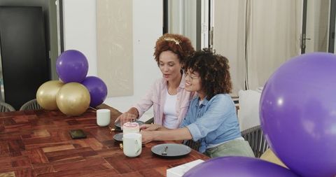African american friends celebrating birthday with cake and purple gold balloons at home