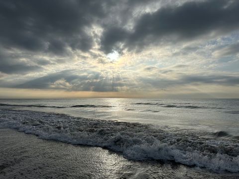 Sunbeams Breaking Through Dramatic Clouds Over Calm Shoreline with Rolling Waves