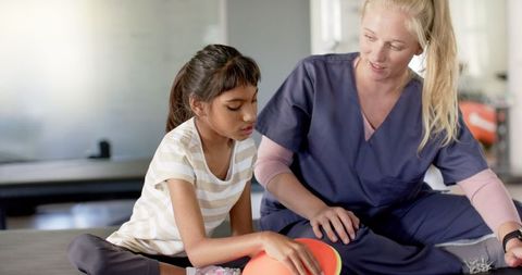Girl in rehabilitation therapy with caring specialist guiding motor skills