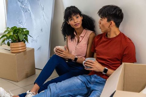 Young couple relaxing while unpacking apartment holding coffee mugs during move