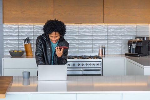 African american man working remotely from sleek kitchen island with laptop and smartphone