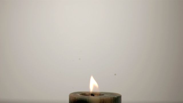 Close-up view of a candle with a tiny flame, capturing a fuel drop falling in super slow motion. This scene beautifully emphasizes the delicate interaction between the drop and the flame, illustrating concepts of ignition, energy or fire safety. Useful for educational materials, inspirational content, meditation and mindfulness platforms, or illustrating scientific principles around combustion and energy transfer.