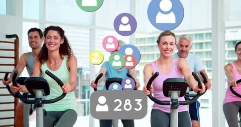 Indoor cycling class with smiling women and men pedaling on spin bikes with social overlay