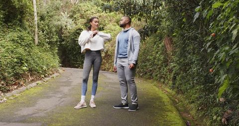 Couple pausing on mossy trail adjusting workout clothes and stretching during outdoor walk