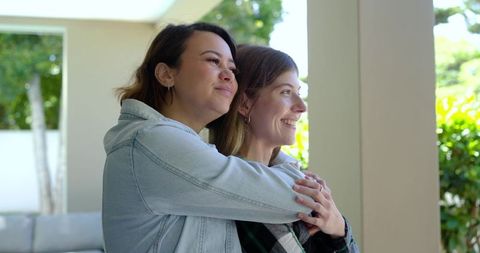 Smiling friends hugging on sunlit porch embracing togetherness and warm outdoor lifestyle