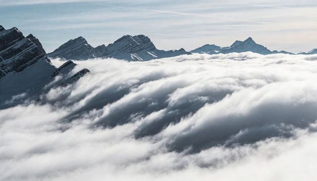 Rolling cloud inversion over snow-clad alpine peaks with sweeping fog-filled valleys
