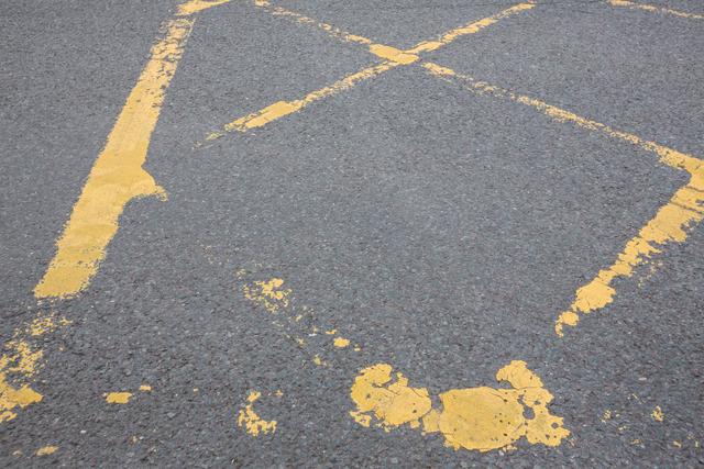 Close-up view of worn yellow road markings on an asphalt surface. Useful for illustrating concepts related to urban infrastructure, transportation, road safety, and the passage of time. Ideal for use in articles, presentations, and educational materials about traffic management, road maintenance, and urban planning.