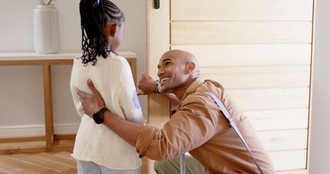 African american father kneeling at front door holding daughter's hand smiling warmly