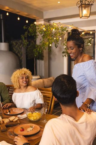 Friends laughing and enjoying outdoor evening dinner on lantern-lit patio