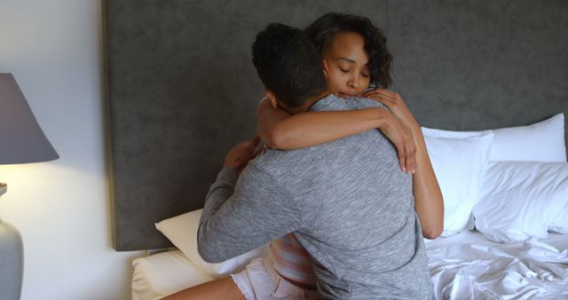 African American couple sharing an affectionate embrace in a cozy bedroom setting, with copy space. Their warm hug conveys a sense of love, comfort, and intimacy between them.