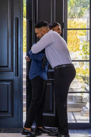 Two african men embracing in sunlit home entryway wearing dress shirts and loafers