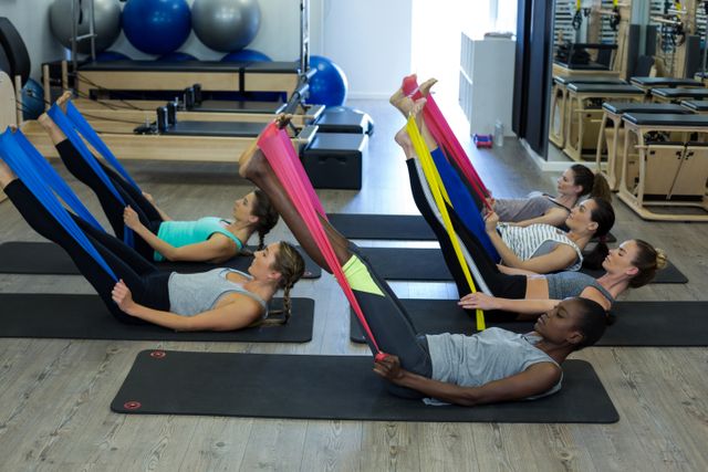 Women in a gym class stretching with resistance bands. Ideal for promoting fitness classes, gym memberships, exercise equipment, and healthy lifestyles. Suitable for use in advertisements, fitness blogs, and wellness websites.